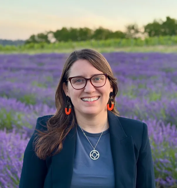 Lauren Tilton, smiling, in a dark blazer in front of a lavender field